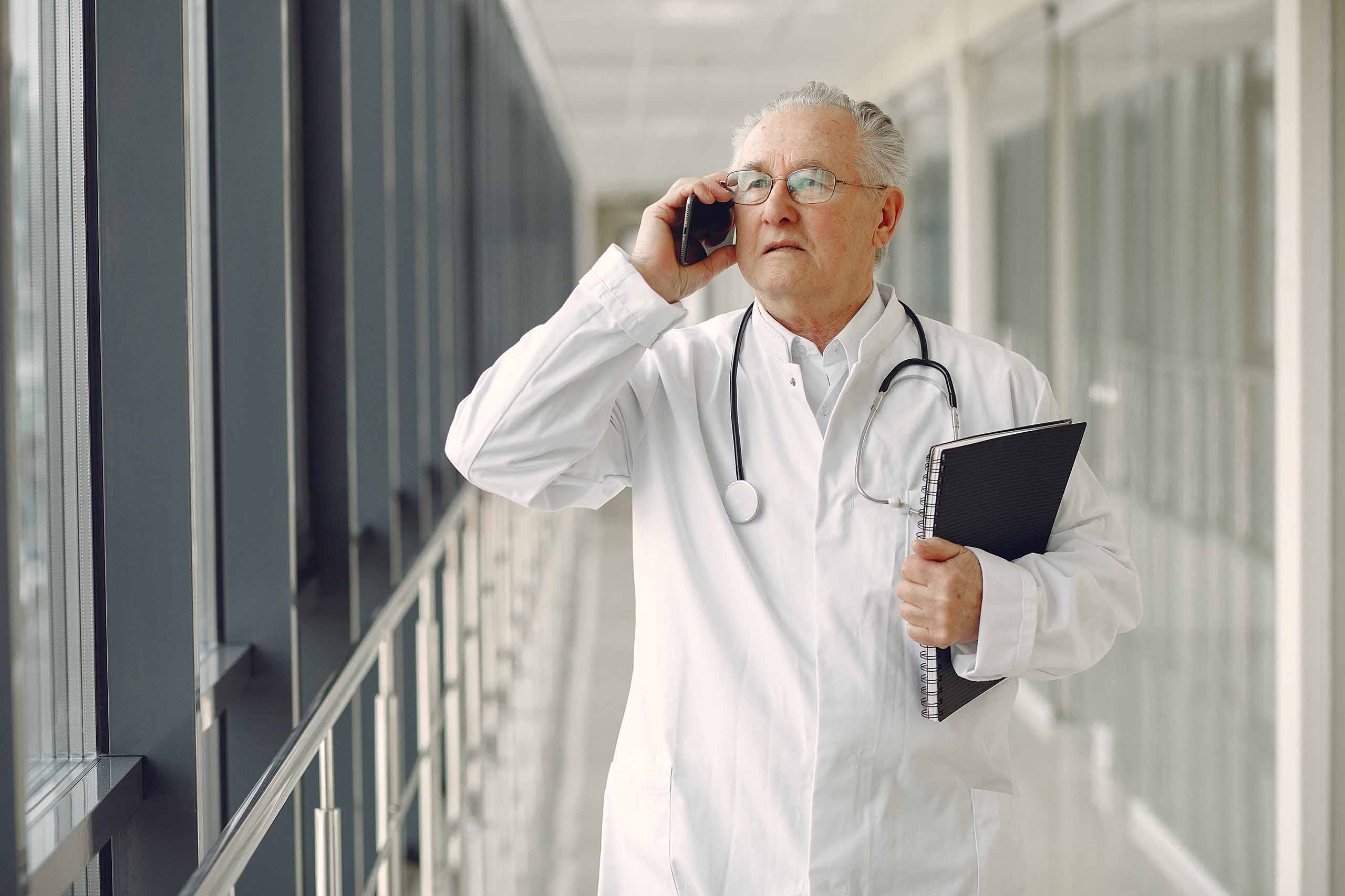Elderly doctor in a white coat with stethoscope talks on phone - www.mysoutherninsurance.com