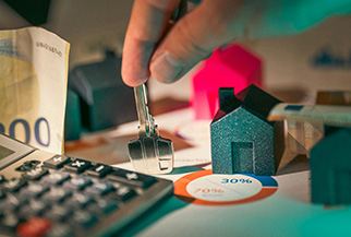 A hand holds keys over miniature houses on charts with a calculator and euro notes nearby - www.mysoutherninsurance.com