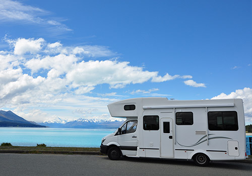 A white camper van is parked beside a vibrant blue lake - www.mysoutherninsurance.com