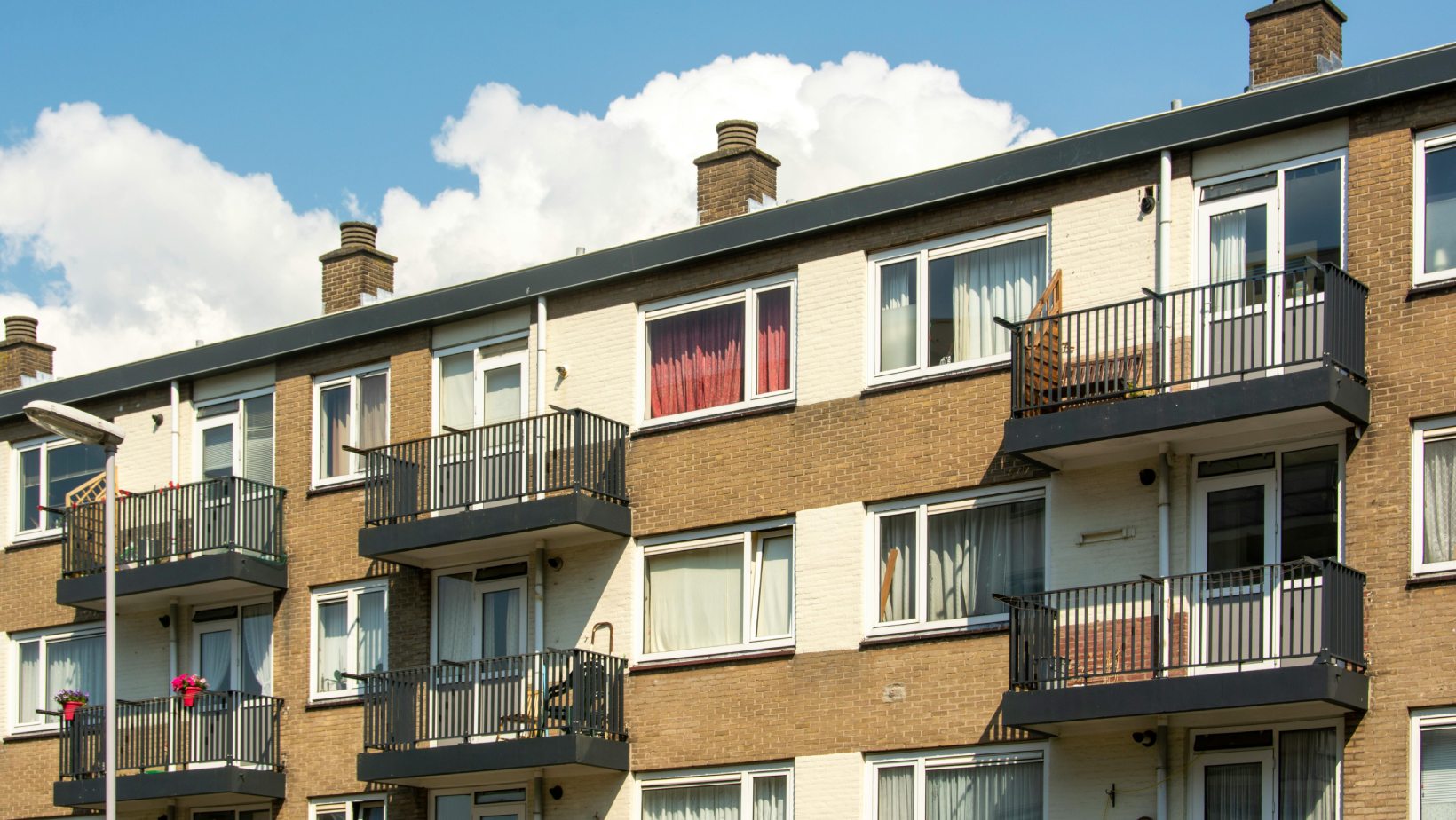 Modern apartment building with balconies and large windows under a bright blue sky - www.mysoutherninsurance.com