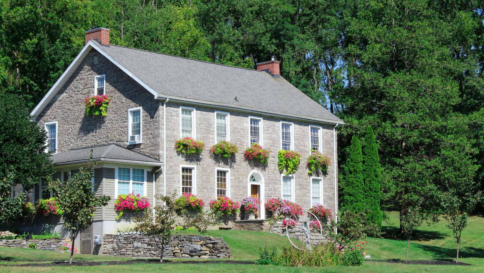 Charming stone house with flower boxes and landscaped garden surrounded by trees on a sunny day - www.mysoutherninsurance.com
